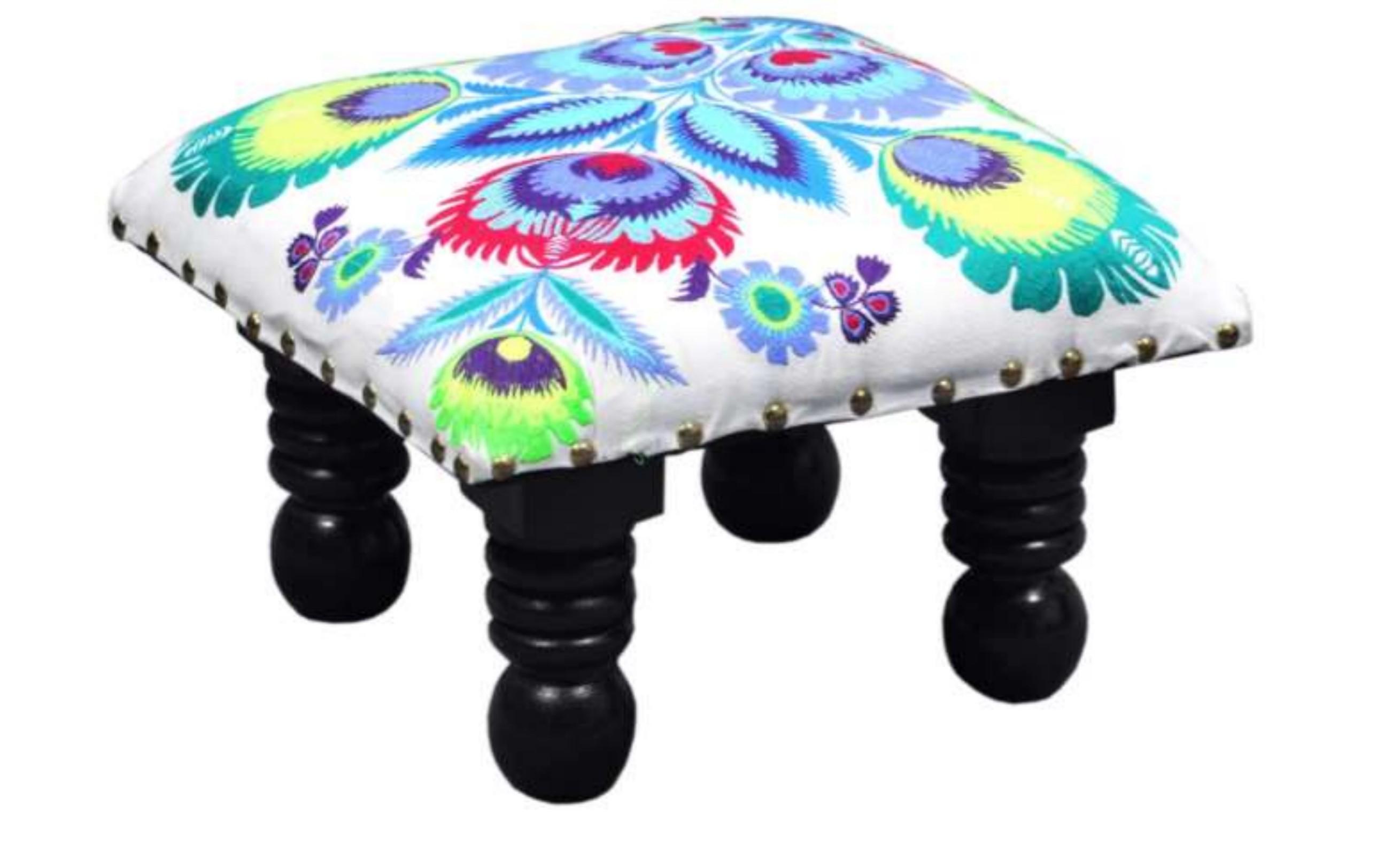 A lively stool adorned with a colorful peacock print accentuated by its natural and sturdy wooden legs, Colorful peacock footstool with hand-painted design, Indian artisanal wooden footstool with peacock motif, Fair trade peacock footstool for living room decor